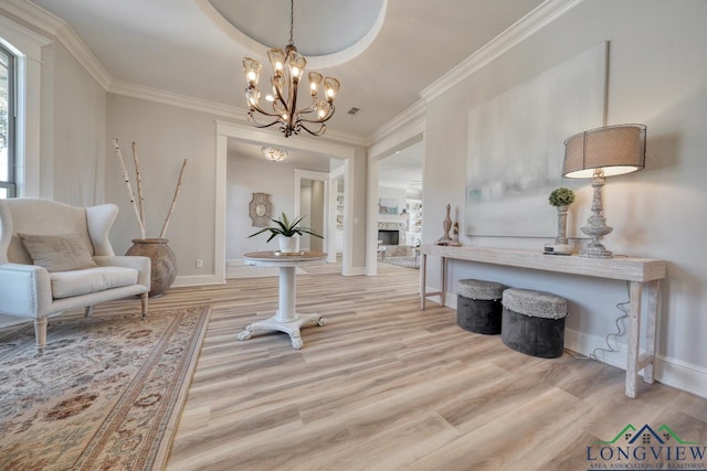 living area featuring a notable chandelier, crown molding, a stone fireplace, and light hardwood / wood-style floors