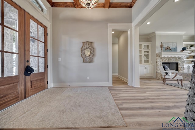 foyer featuring french doors, beam ceiling, ornamental molding, a fireplace, and light hardwood / wood-style floors