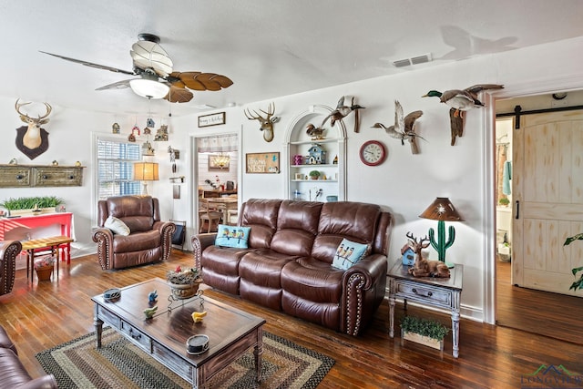 living room featuring dark wood-type flooring, ceiling fan, and a barn door