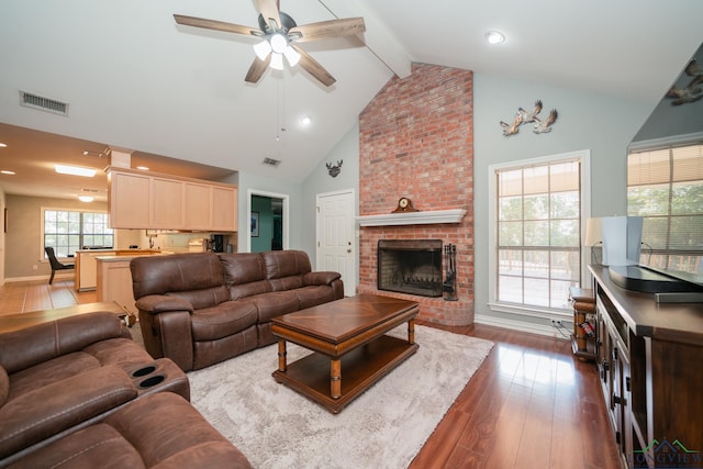 living room featuring dark wood-type flooring, high vaulted ceiling, ceiling fan, a fireplace, and beamed ceiling