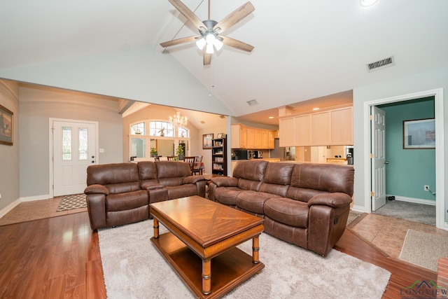 living room with ceiling fan with notable chandelier, vaulted ceiling with beams, and light wood-type flooring