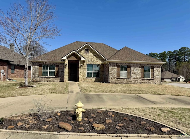 craftsman-style home with brick siding, a shingled roof, and a front yard