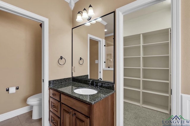 bathroom featuring tile patterned floors, a walk in closet, toilet, baseboards, and vanity