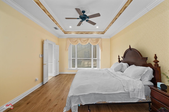 bedroom with ceiling fan, a raised ceiling, crown molding, and light hardwood / wood-style flooring