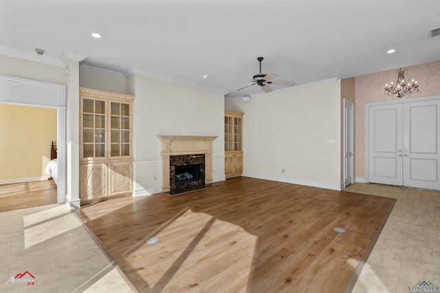 unfurnished living room with crown molding, a fireplace, ceiling fan with notable chandelier, and light wood-type flooring