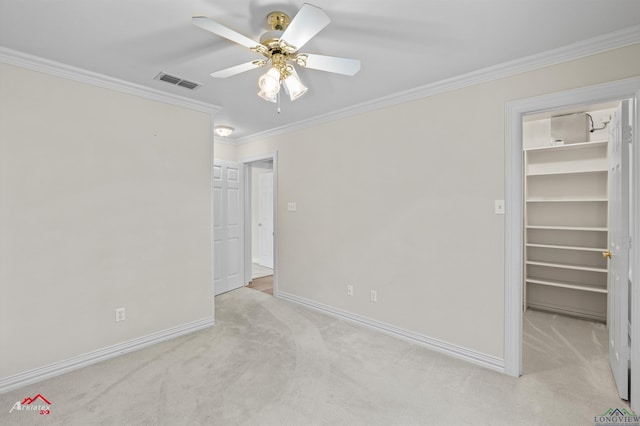 unfurnished bedroom featuring a walk in closet, ceiling fan, light colored carpet, and ornamental molding