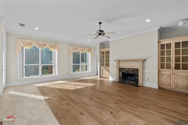 unfurnished living room featuring a high end fireplace, light wood-type flooring, ceiling fan, and ornamental molding