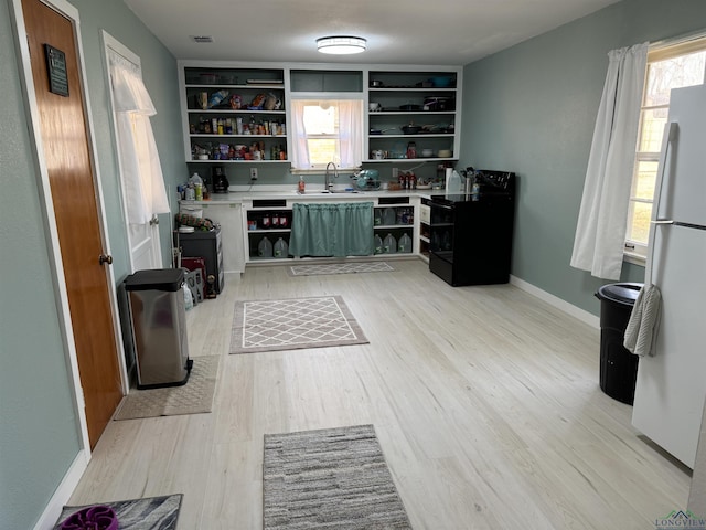 bar featuring black electric range oven, sink, white fridge, plenty of natural light, and light wood-type flooring