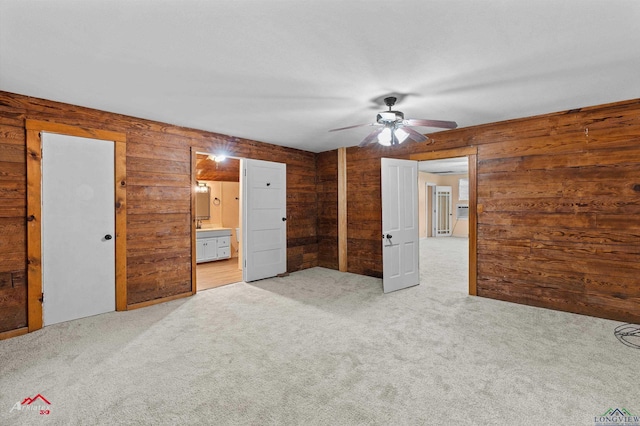 154 County Rd 117, Carthage, TX 75633 - unfurnished bedroom featuring light carpet, wooden walls, connected bathroom, and ceiling fan