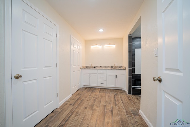 full bathroom featuring a sink, wood finished floors, a tile shower, double vanity, and baseboards