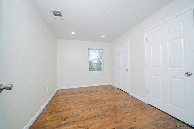 unfurnished bedroom featuring visible vents, baseboards, recessed lighting, wood finished floors, and a textured ceiling