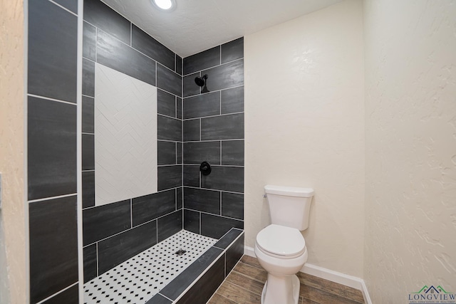 full bath featuring wood finish floors, toilet, baseboards, and tiled shower