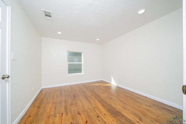 empty room featuring visible vents, a textured ceiling, wood finished floors, recessed lighting, and baseboards