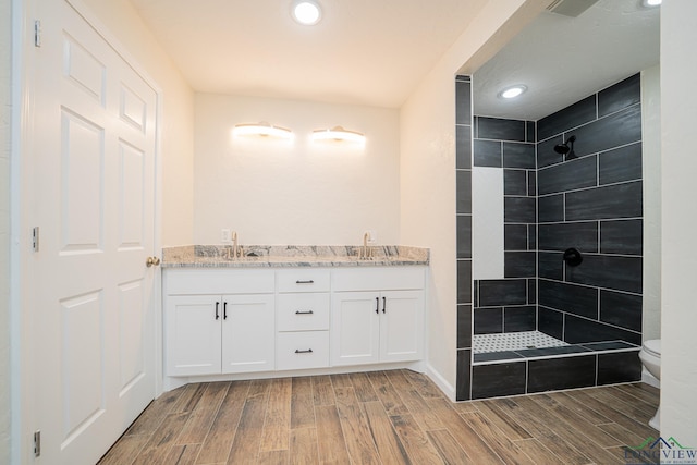 bathroom featuring wood finish floors, toilet, a sink, and a tile shower