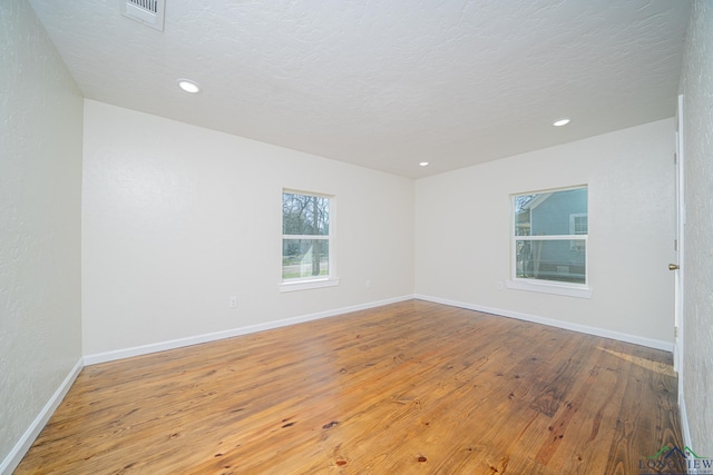 unfurnished room featuring hardwood / wood-style floors, baseboards, visible vents, and a textured ceiling