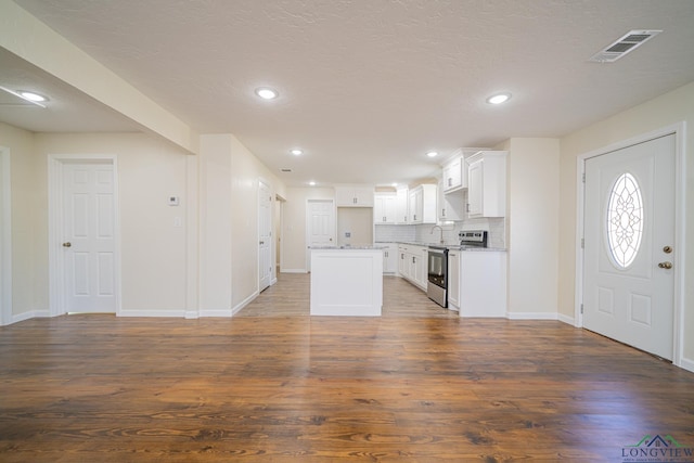 kitchen with visible vents, stainless steel range with electric stovetop, tasteful backsplash, wood finished floors, and white cabinetry