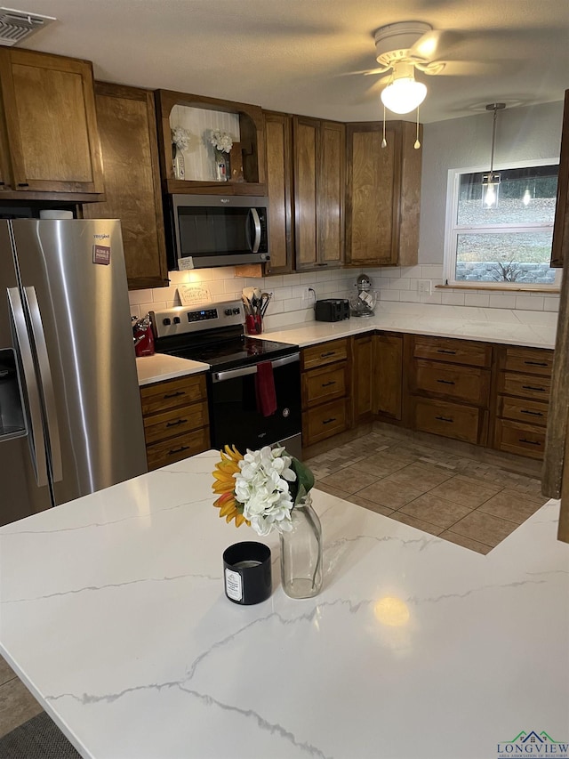 kitchen with ceiling fan, light stone countertops, appliances with stainless steel finishes, tasteful backsplash, and decorative light fixtures