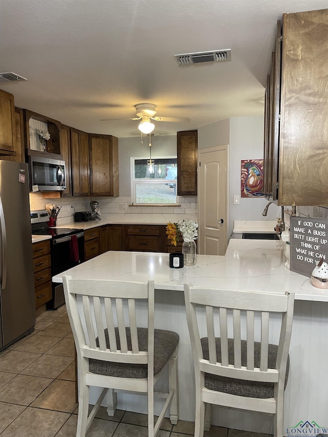 kitchen featuring backsplash, sink, light tile patterned floors, kitchen peninsula, and stainless steel appliances