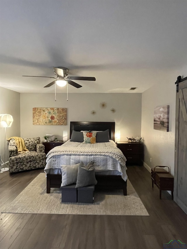 bedroom featuring dark hardwood / wood-style flooring, a barn door, and ceiling fan