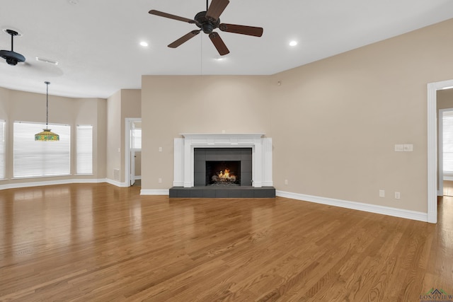 unfurnished living room featuring hardwood / wood-style flooring, ceiling fan, and a tiled fireplace