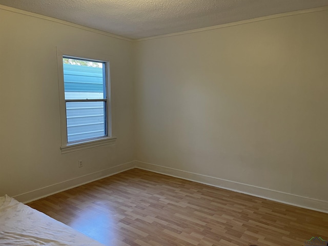 spare room featuring crown molding, a textured ceiling, and light wood-type flooring