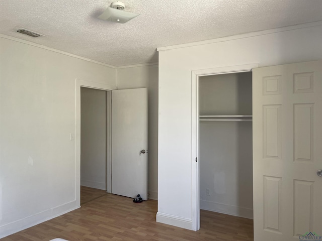 unfurnished bedroom with a closet, ornamental molding, a textured ceiling, and light hardwood / wood-style flooring