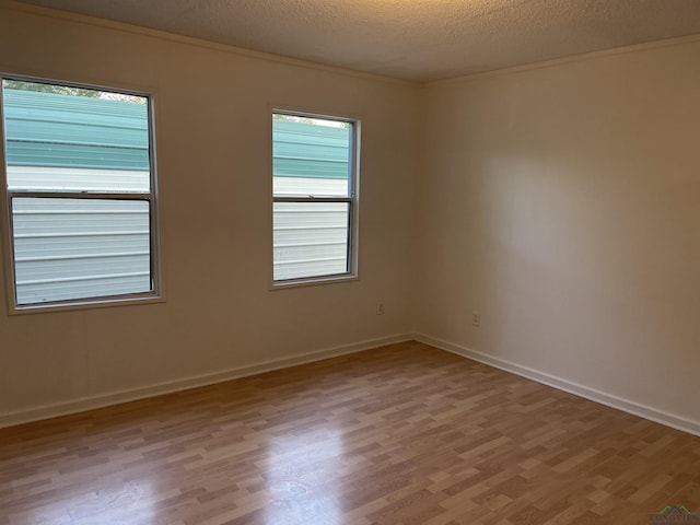 empty room featuring crown molding, a textured ceiling, and light wood-type flooring