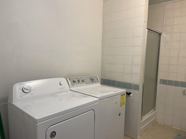 clothes washing area featuring washing machine and dryer, light tile patterned floors, and tile walls