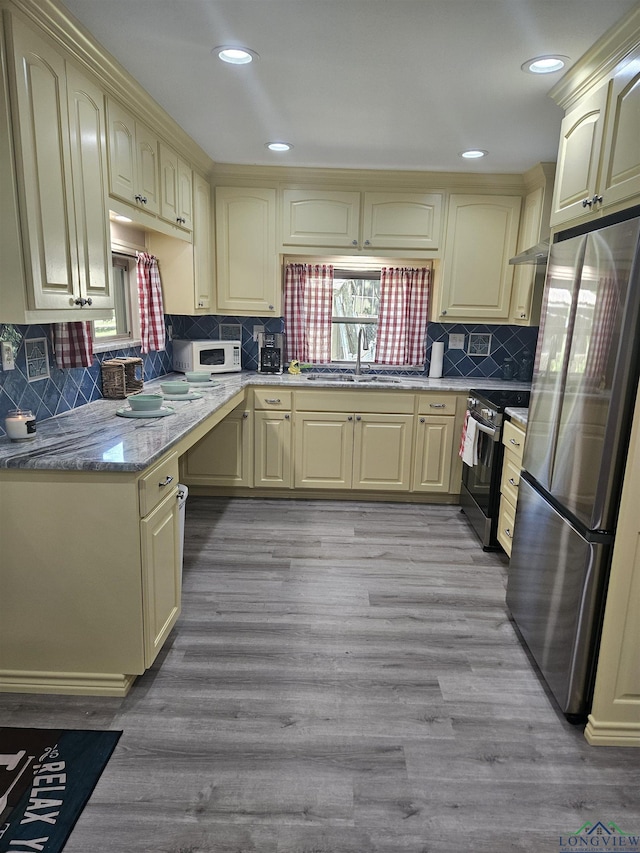 kitchen featuring backsplash, sink, appliances with stainless steel finishes, light hardwood / wood-style floors, and light stone counters