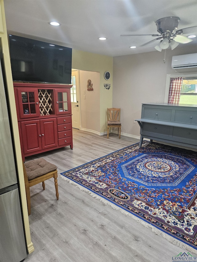 living area with an AC wall unit, ceiling fan, and light hardwood / wood-style flooring