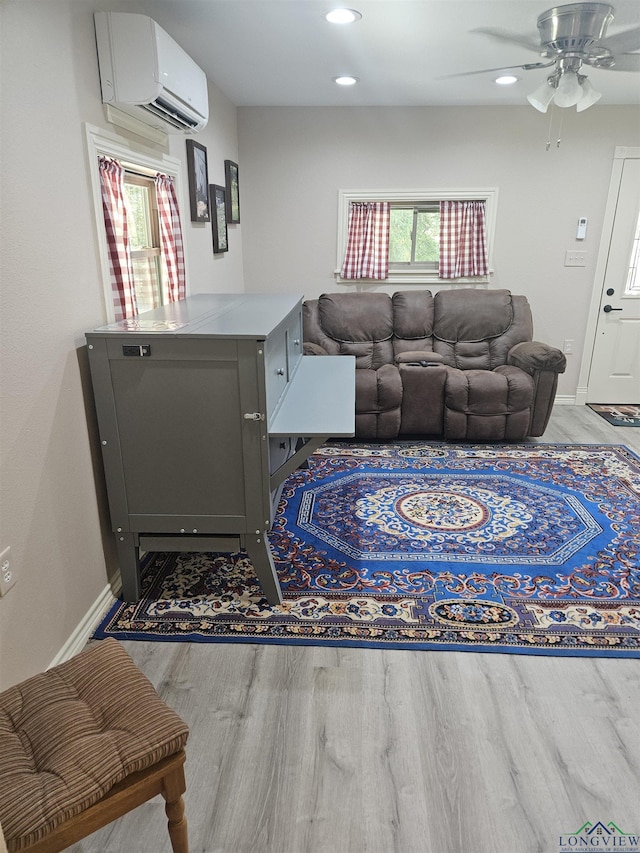 living room featuring a wall mounted air conditioner, light wood-type flooring, and ceiling fan