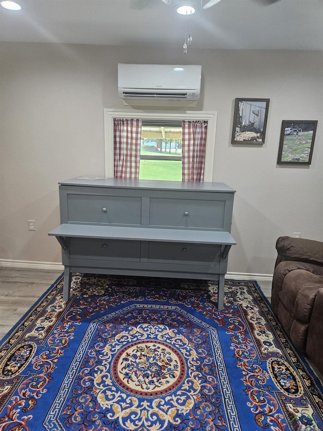 sitting room with hardwood / wood-style flooring, ceiling fan, and an AC wall unit