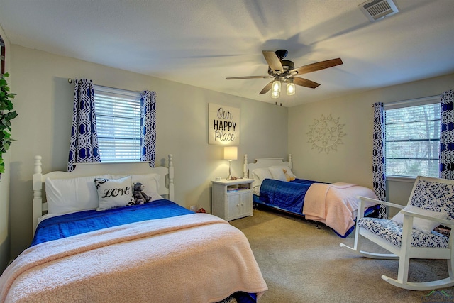 bedroom with ceiling fan, multiple windows, visible vents, and light colored carpet