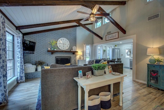 living area with a healthy amount of sunlight, a brick fireplace, light wood-type flooring, and visible vents