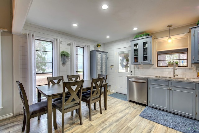 kitchen featuring a sink, hanging light fixtures, stainless steel dishwasher, light stone countertops, and glass insert cabinets