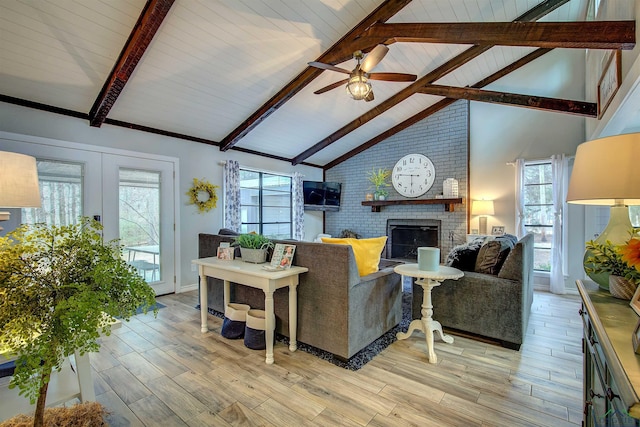 living area featuring a ceiling fan, french doors, light wood-type flooring, a fireplace, and beam ceiling