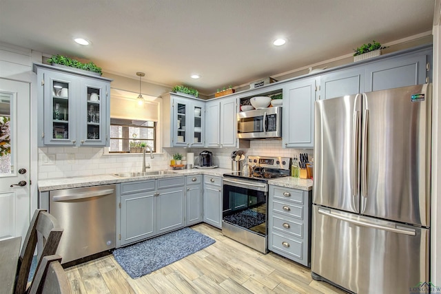 kitchen featuring glass insert cabinets, pendant lighting, stainless steel appliances, and a sink