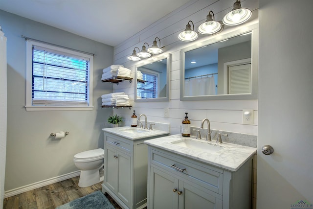 full bath featuring baseboards, two vanities, a sink, and wood finished floors