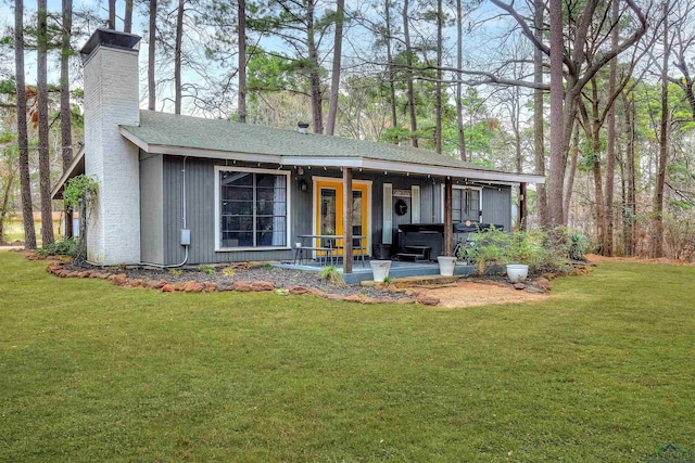 back of house with roof with shingles, a porch, a lawn, and a chimney