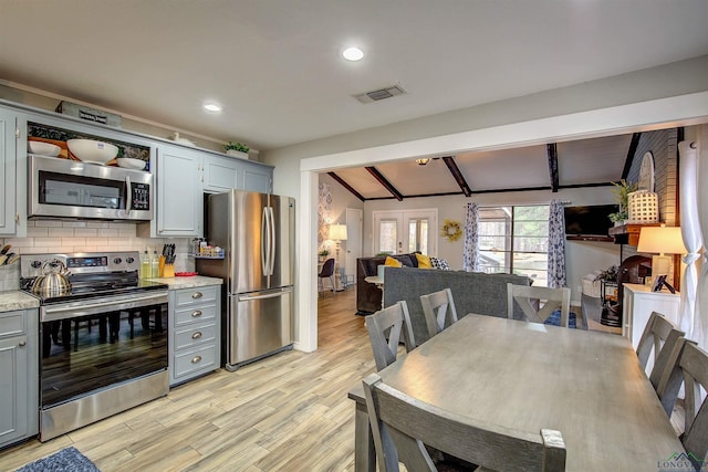 kitchen featuring vaulted ceiling with beams, visible vents, appliances with stainless steel finishes, decorative backsplash, and light wood finished floors