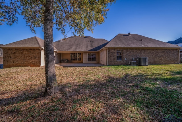 back of property with a shingled roof, brick siding, cooling unit, a patio, and a yard