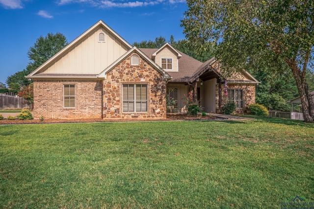 view of front of property with fence, a front yard, stone siding, a shingled roof, and board and batten siding