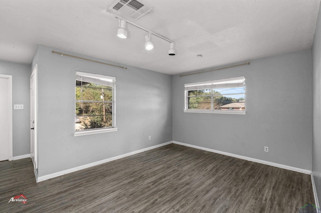 empty room featuring a wealth of natural light, rail lighting, and dark wood-type flooring