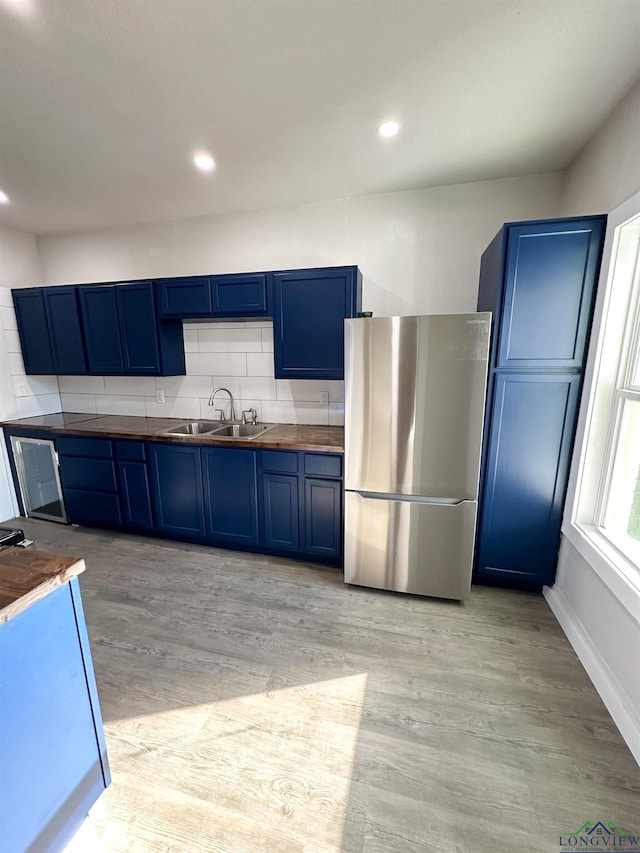 kitchen featuring blue cabinets, stainless steel fridge, sink, and light wood-type flooring