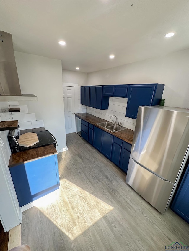 kitchen with sink, light hardwood / wood-style flooring, wooden counters, stainless steel refrigerator, and blue cabinets