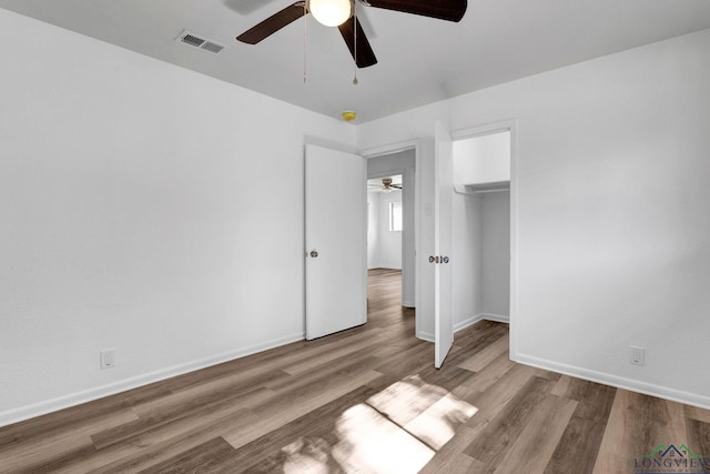 unfurnished bedroom with light wood-type flooring, a closet, a spacious closet, and ceiling fan