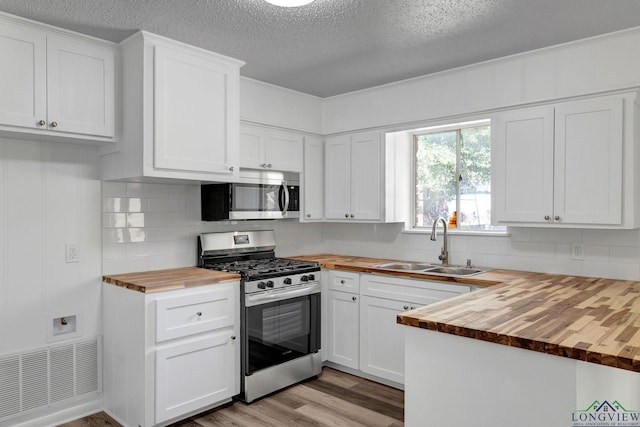 kitchen with wood counters, sink, a textured ceiling, white cabinetry, and stainless steel appliances