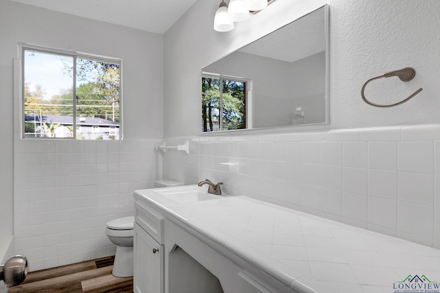 bathroom with plenty of natural light, vanity, hardwood / wood-style floors, and tile walls