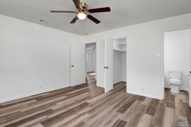 unfurnished bedroom featuring ceiling fan, a spacious closet, connected bathroom, wood-type flooring, and a closet