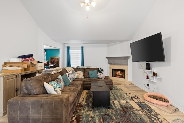 living room with a tile fireplace, ceiling fan, lofted ceiling, and light wood-type flooring